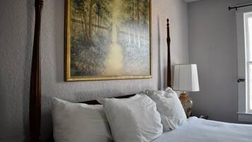 Un dormitorio con una cama grande, una mesita de noche con lámpara y un cuadro de un paisaje boscoso en la pared.