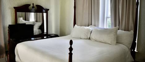 A bedroom with a large bed, a wooden headboard, a nightstand, a mirror, and a window with curtains.