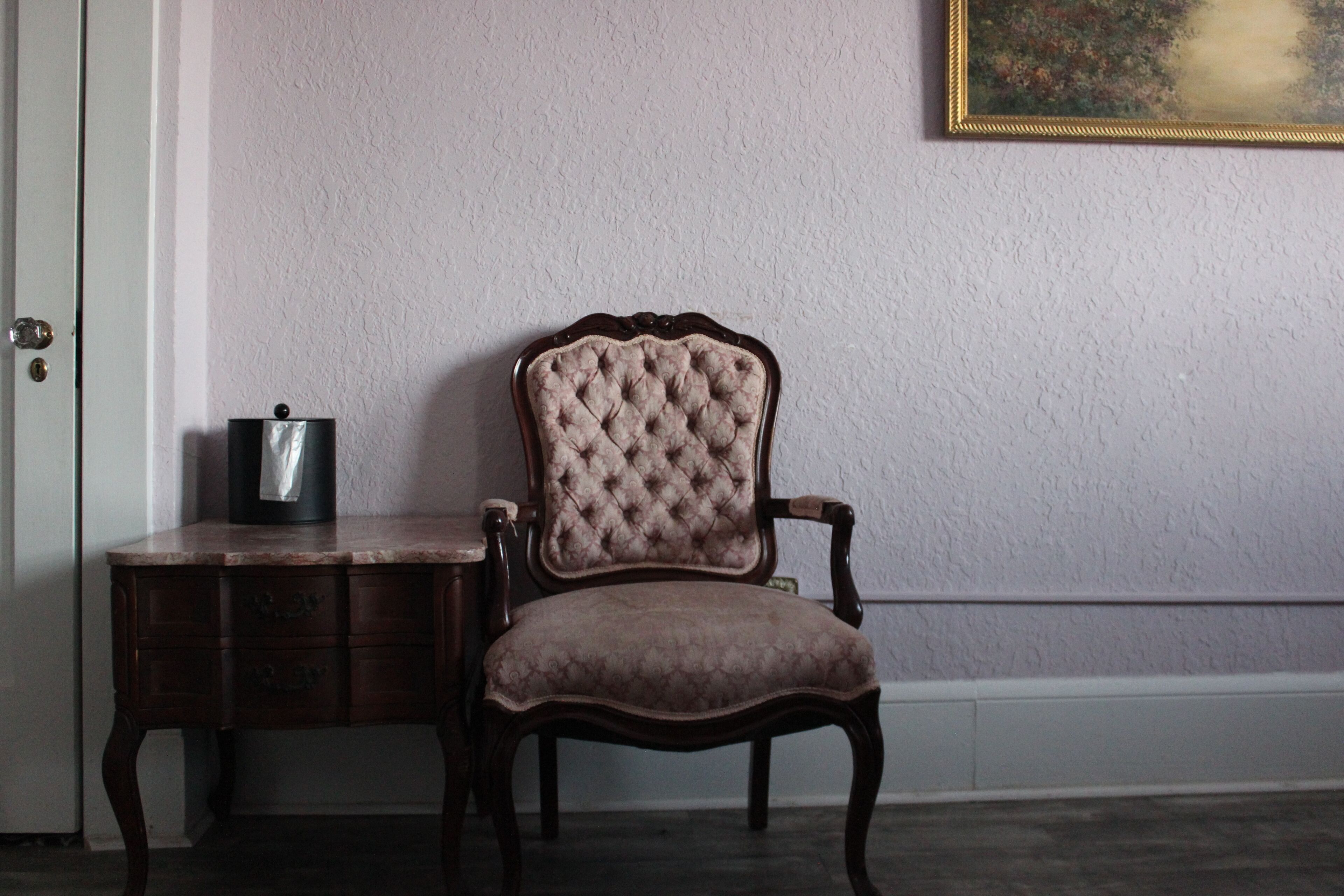 Une chaise dotée d’un dossier capitonné et d’un siège rembourré, placée à côté d’une table d’appoint en bois sur laquelle se trouve un objet noir.