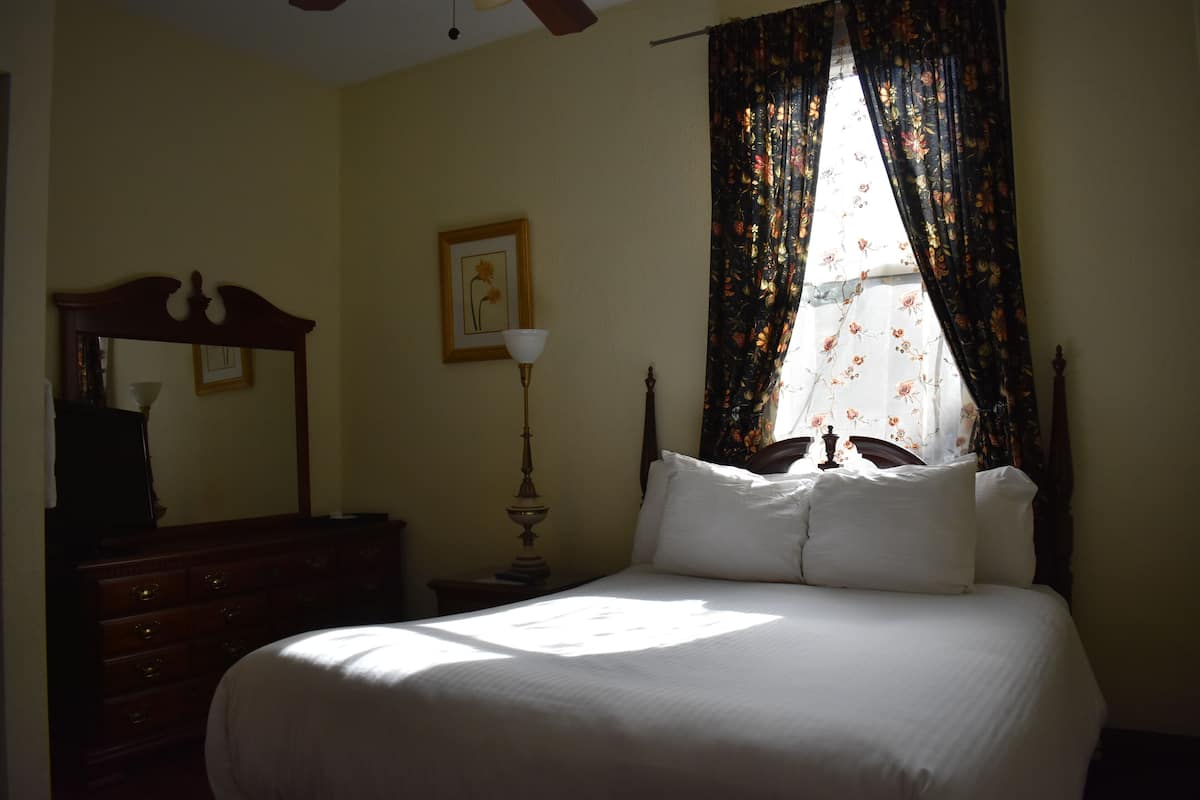 A bedroom with a bed, a dresser, a lamp, and a window with floral curtains.