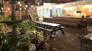 An outdoor patio area with a wooden bench, a stone fountain, and string lights. - The DeLand Hotel (DeLand)