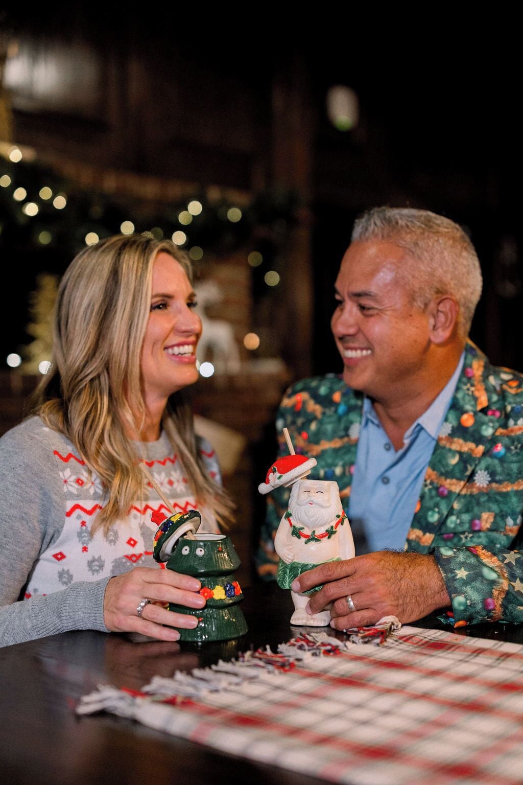 Dos personas sosteniendo adornos festivos sobre una mesa con mantel a cuadros.