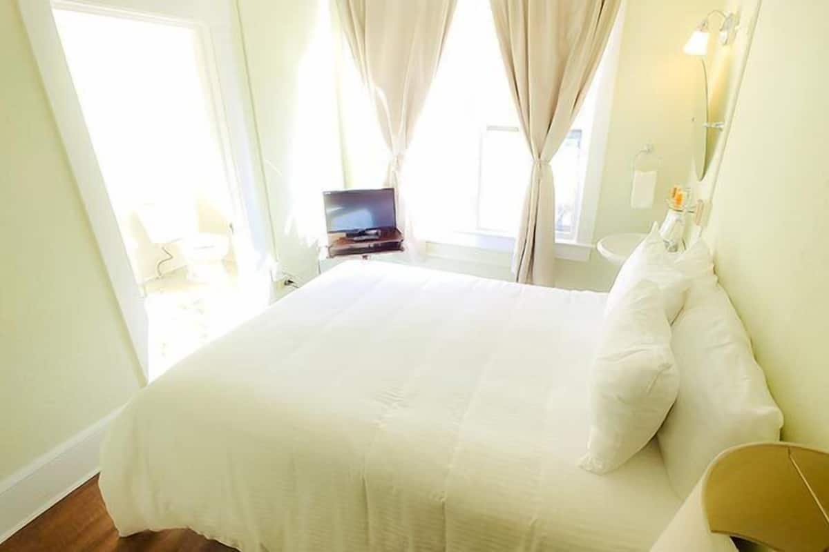A hotel room with a bed, a television, a bedside table, and a bathroom visible through an open door.