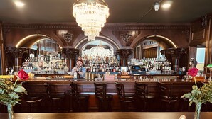 A bar with a wooden counter, bar stools, and a chandelier. - The DeLand Hotel (DeLand)