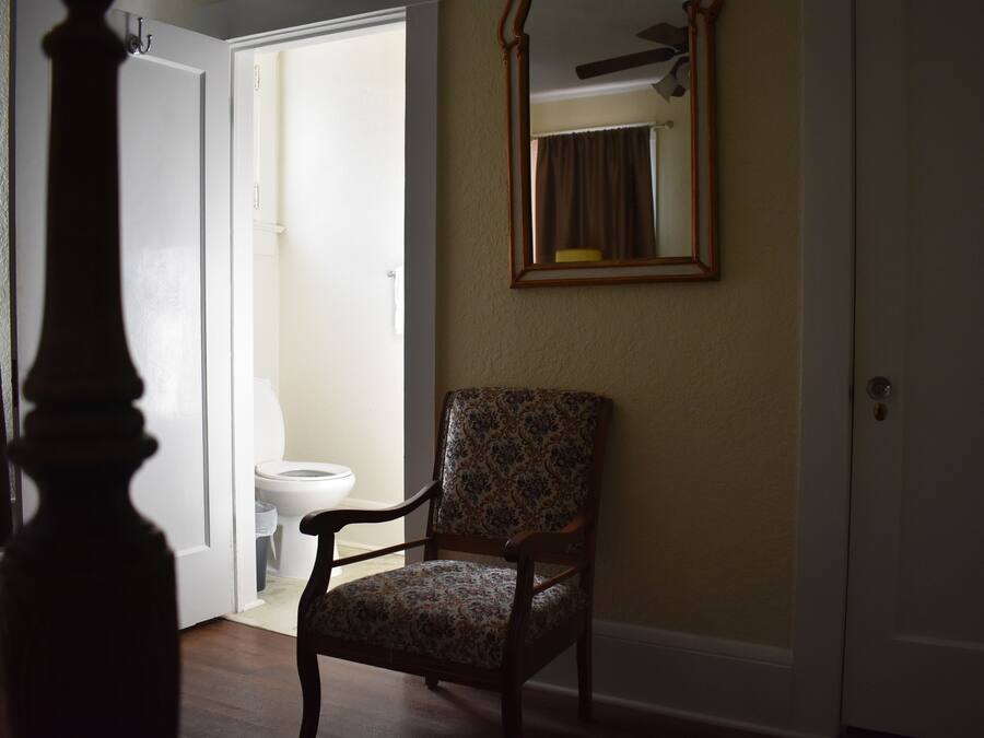 A room with a wooden chair, a ceiling fan, and a door leading to a bathroom.