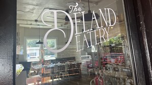 A storefront with the sign "The Deland Eatery" and a display of various bottles and glasses inside. - The DeLand Hotel (DeLand)