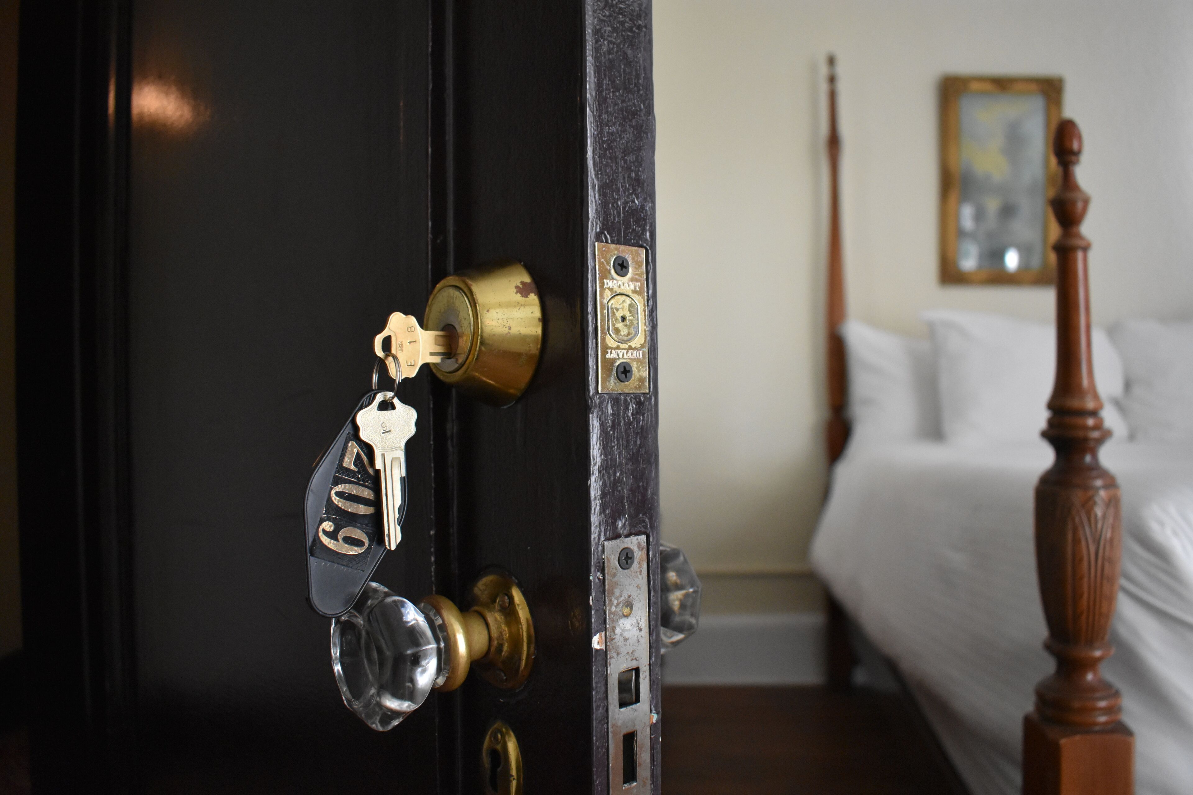 A door with a brass lock and a key, a bed with a wooden headboard, and a framed picture on the wall.