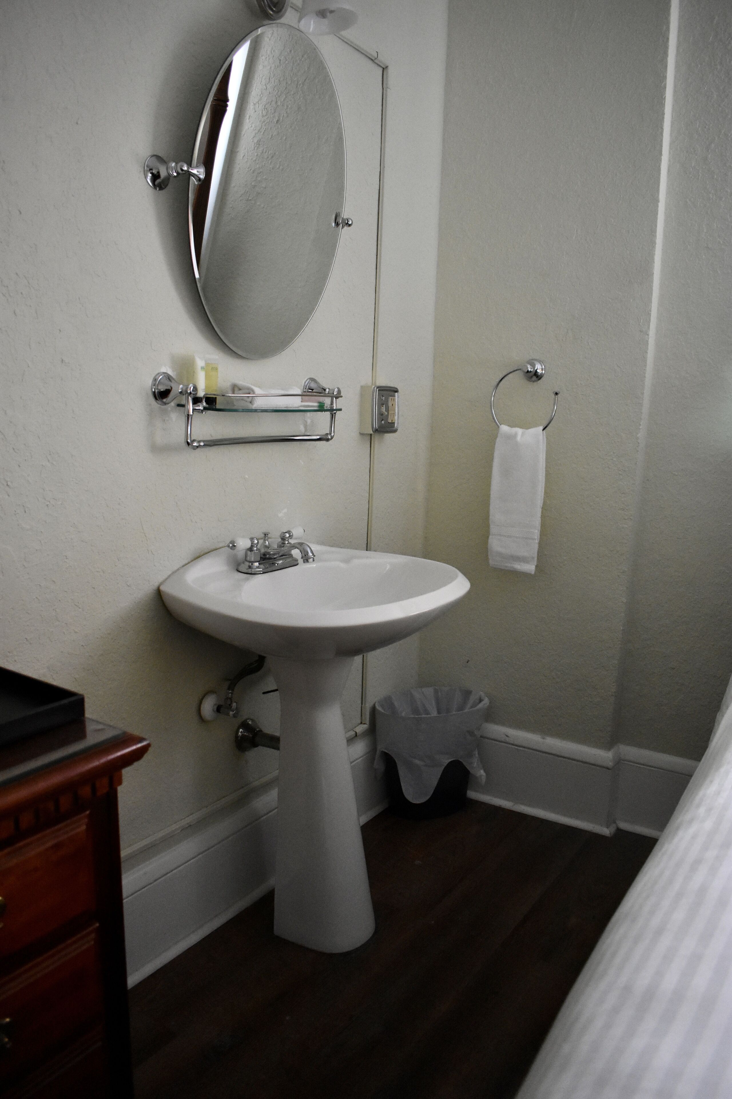 Un baño con lavamanos blanco, espejo, toallero y cubo de basura.