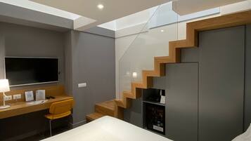 A modern bedroom with a bed, a desk with a chair, a TV, and a staircase.