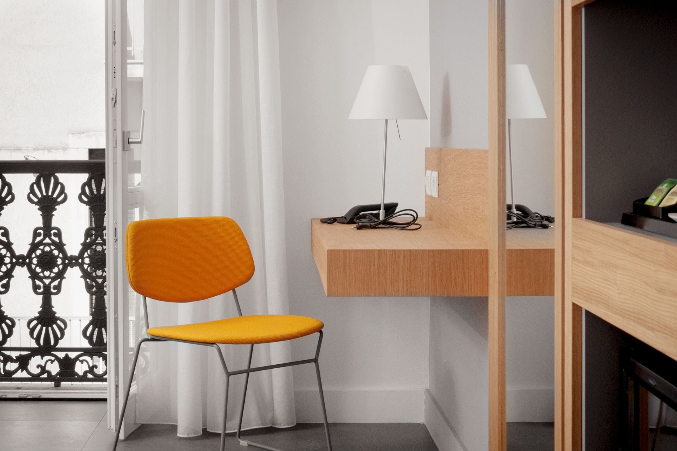 A modern room with a wooden desk, a chair, a lamp, and a phone.