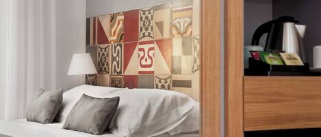 A hotel room with a neatly made bed, a lamp, and a coffee maker on a shelf.
