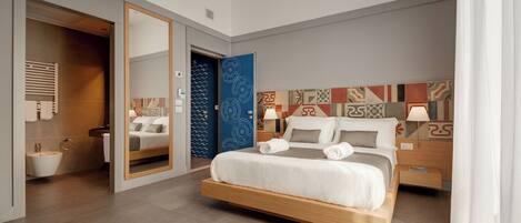 A modern hotel room with a large bed, a bathroom with a sink, and a mirror.