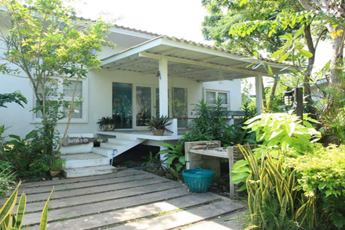 A house with a covered porch, steps leading to the entrance, and various potted plants around the property.