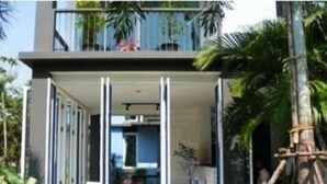 Um edifício moderno com varanda, janelas amplas e vista para o verde ao redor.