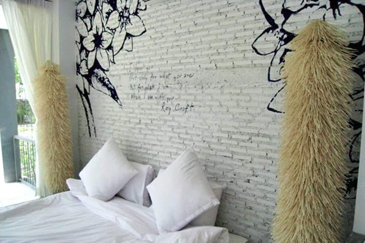 A bedroom with a white brick wall, a floral mural, and two fluffy pillows.