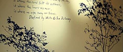 Una habitación con un sillón amarillo, una pared con siluetas de árboles y texto, y un suelo estampado.