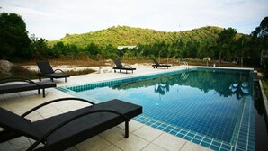 Piscina com espreguiçadeiras e vista para uma colina.