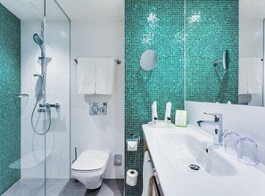 Un baño moderno con cabina de ducha de vidrio, inodoro blanco y lavamanos con dispensadores de jabón de vidrio transparente.