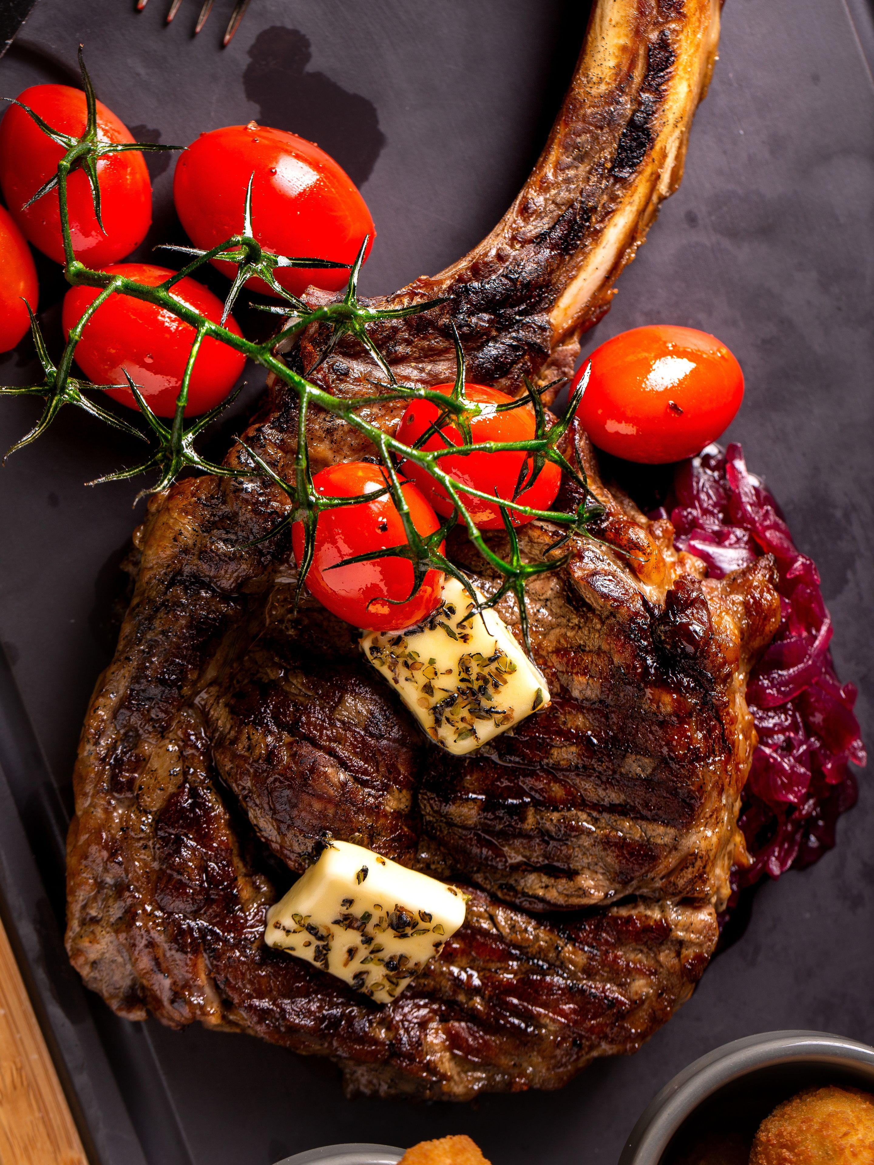 A steak with cherry tomatoes and a pat of butter on a dark plate.