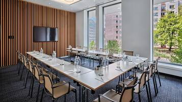 Un salón de conferencias con una larga mesa, sillas, una pantalla de televisión y ventanas amplias con vista a la ciudad.