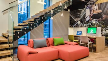 Un interior moderno con una escalera de madera, un sofá modular rojo y un escritorio con una computadora.