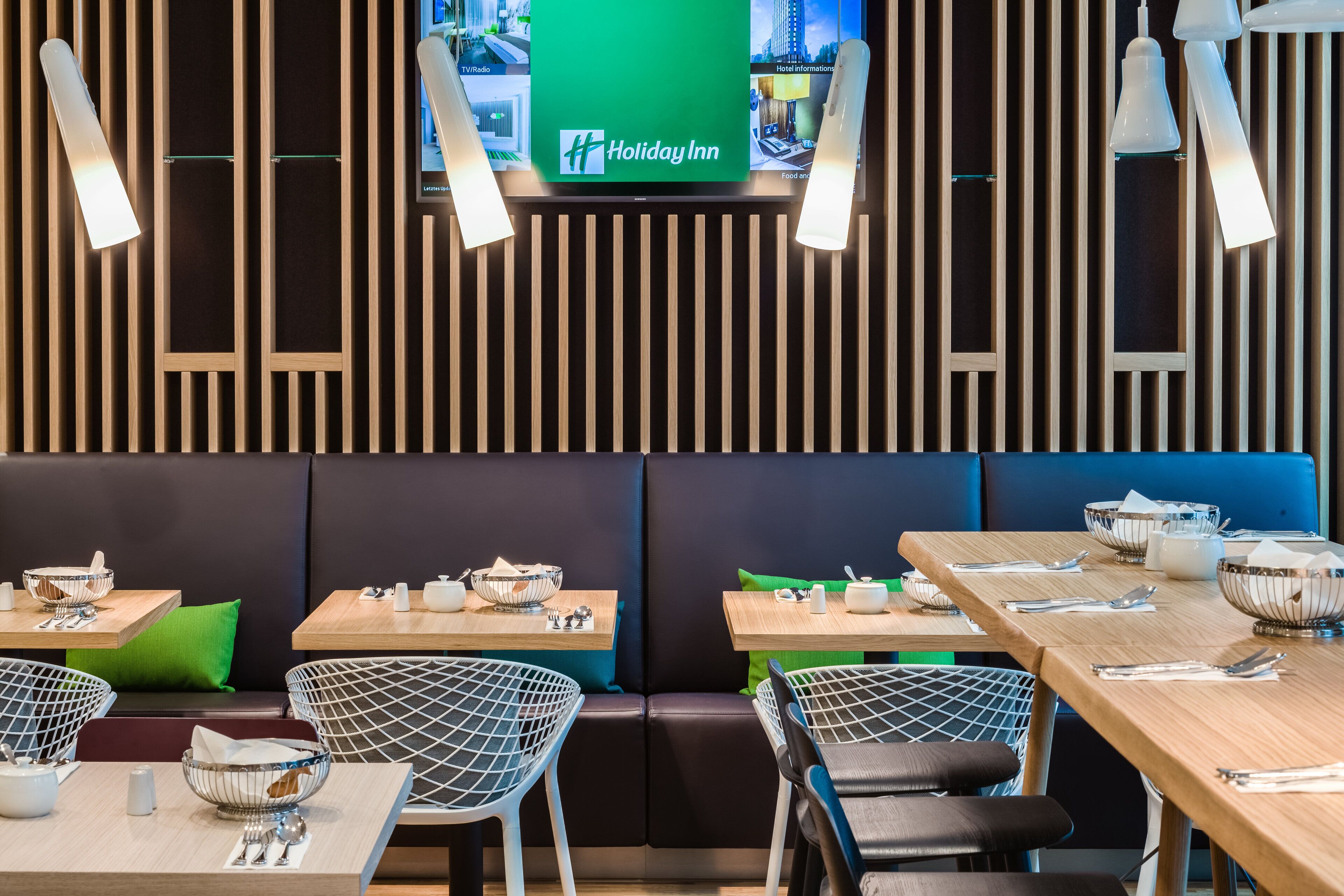 A modern restaurant interior with wooden paneling, black and white wire mesh chairs, and tables set for dining.