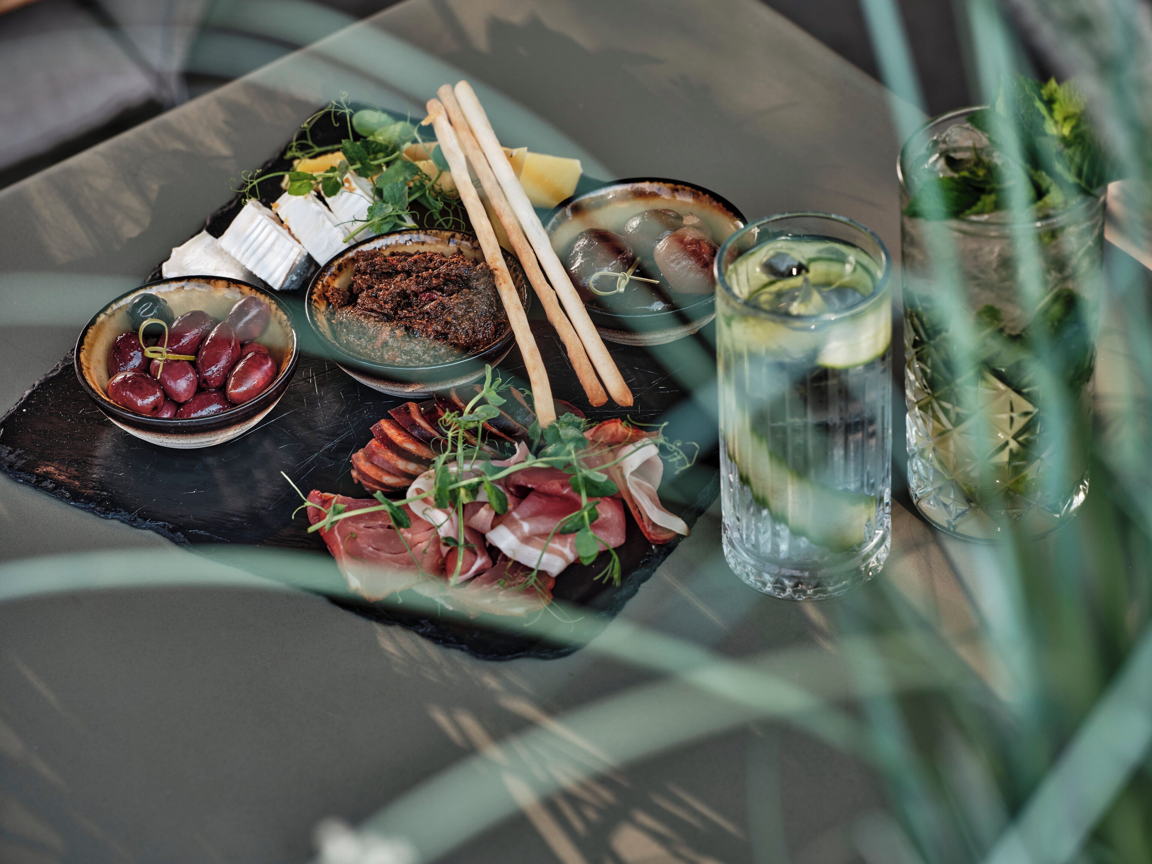 A charcuterie board with various meats, cheeses, and olives on a slate tray.