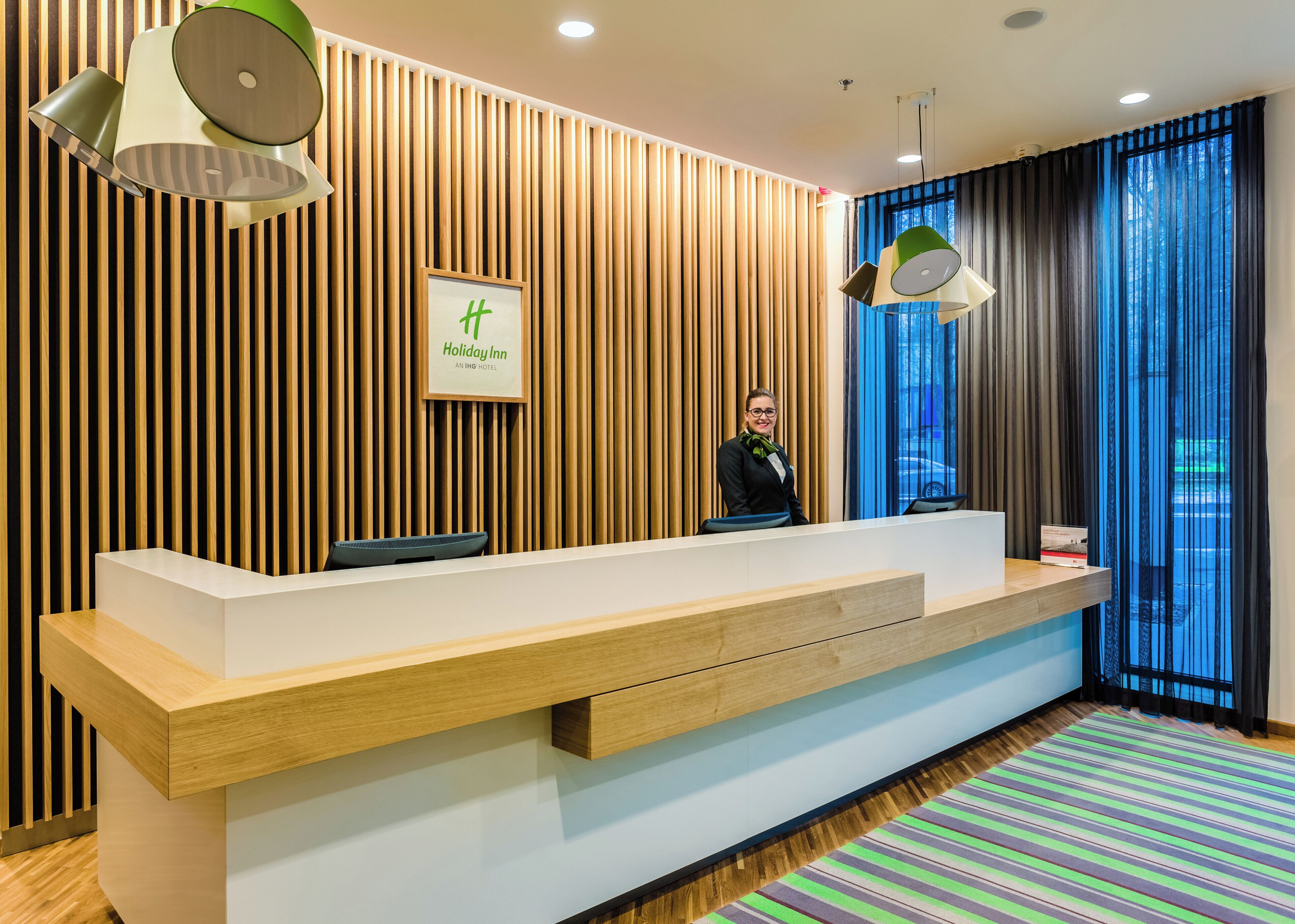 A hotel reception desk with a modern design, a framed sign, and a view through the window.