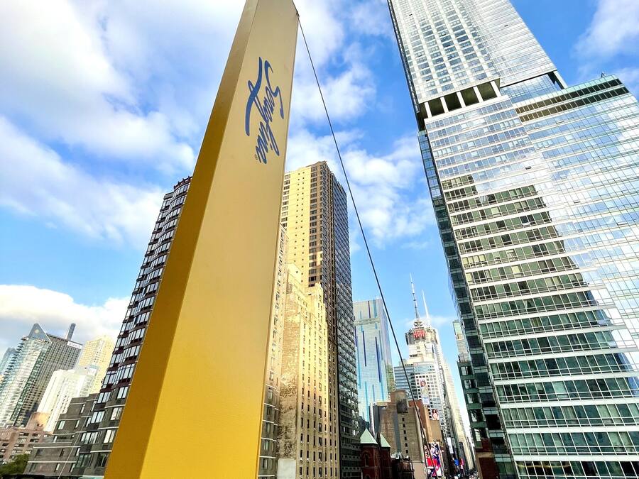 A cityscape with modern high-rise buildings, a prominent yellow structure with a blue logo, and a busy street with vehicles.