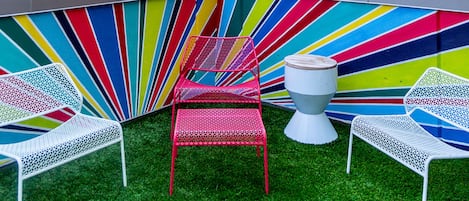 A rooftop terrace with colorful chairs and a view of a city skyline.