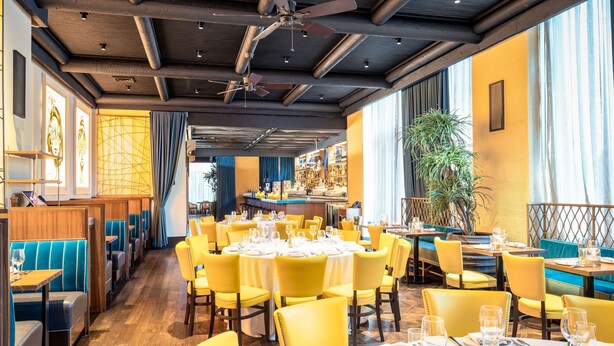 A restaurant with yellow chairs and tables, wooden floors, and a ceiling fan.