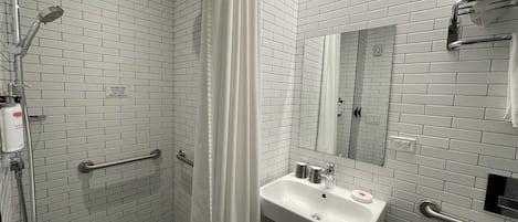 Ein Badezimmer mit weißen Fliesenwänden, einer Duschbank, einem Waschbecken, einem Spiegel und einem Handtuchhalter.