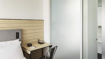 Habitación de hotel con cama, escritorio, silla, armario y baño visible a través de la puerta.
