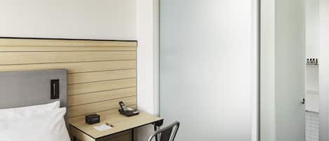 A hotel room with a bed, a desk, a chair, a wardrobe, and a bathroom visible through the door.
