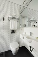 A modern bathroom with white subway tiles, a white toilet, a sink with a mirror, and a towel rack with neatly folded towels.