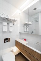A modern bathroom with a white sink, wooden vanity, and a large mirror.