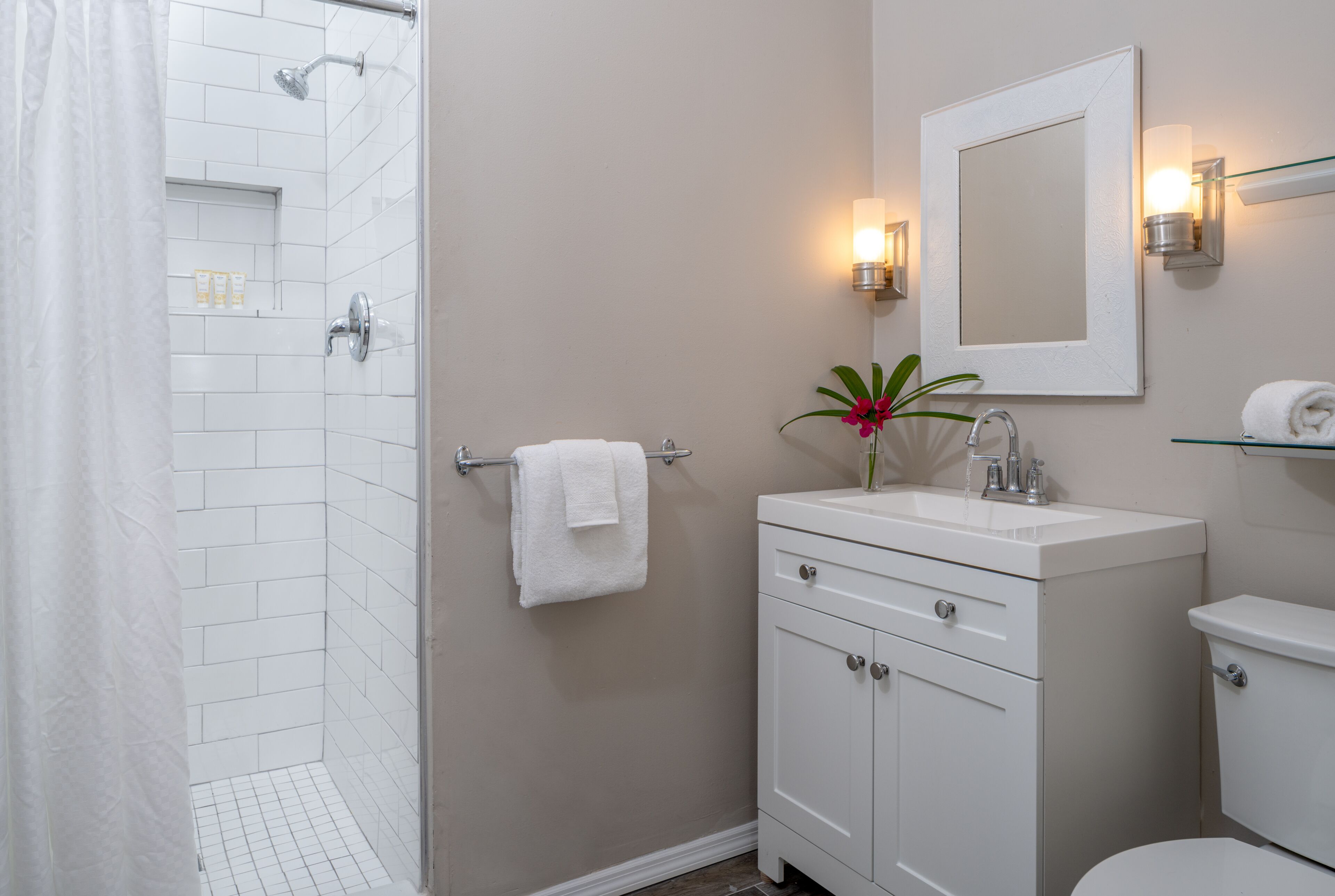 A bathroom with a shower, toilet, sink, and mirror.