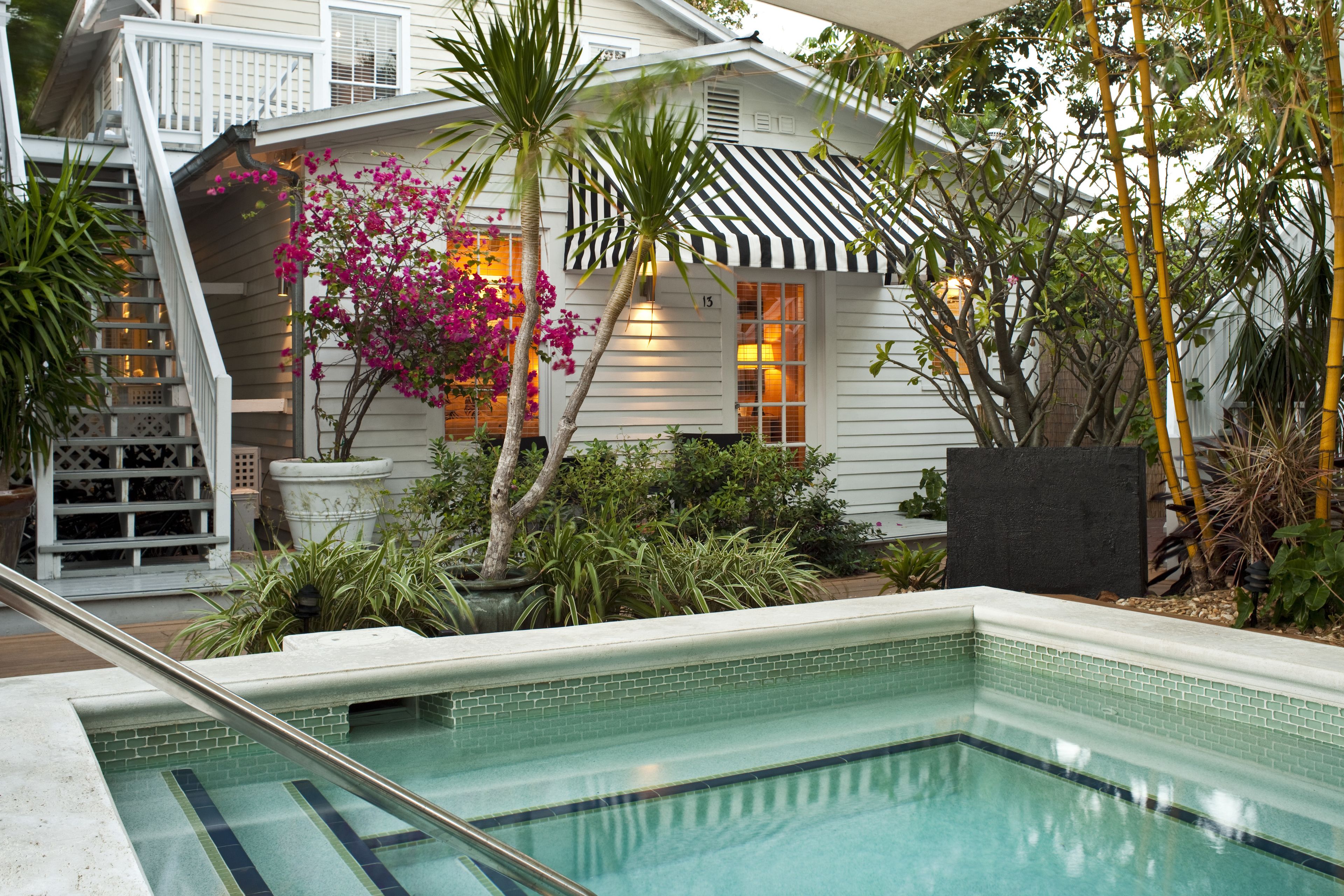 A pool area with a tiled edge, a staircase, and a house with a striped awning.