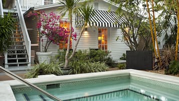 A pool area with a tiled edge, a staircase, and a house with a striped awning.