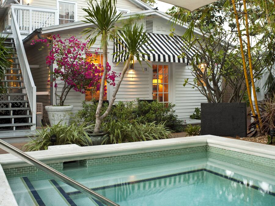 A pool area with a tiled edge, a staircase, and a house with a striped awning.
