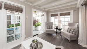 Amplia sala de estar con sofá, sillas y una mesa de comedor. Hay ventanas grandes con persianas, una puerta que da a un patio y un techo con vigas a la vista.