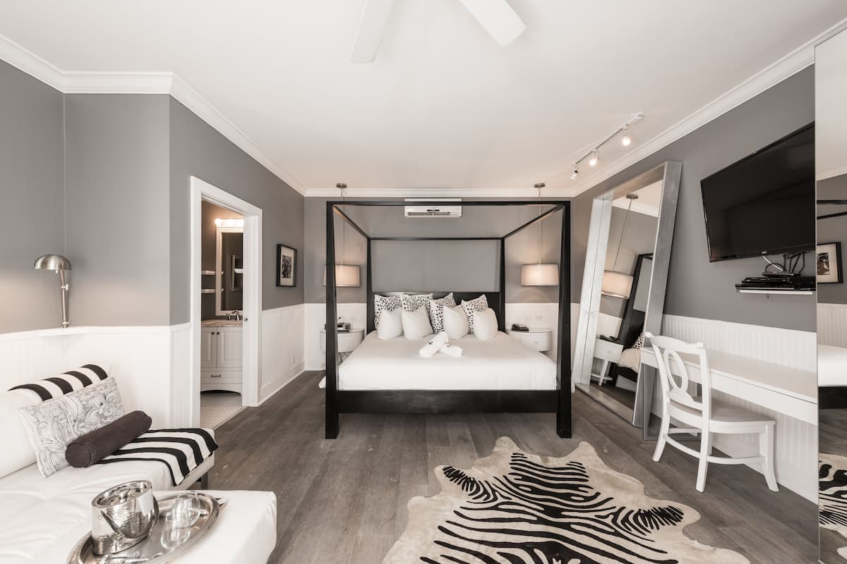 A modern bedroom with a four-poster bed, a zebra-patterned rug, a white desk, and a large mirror.