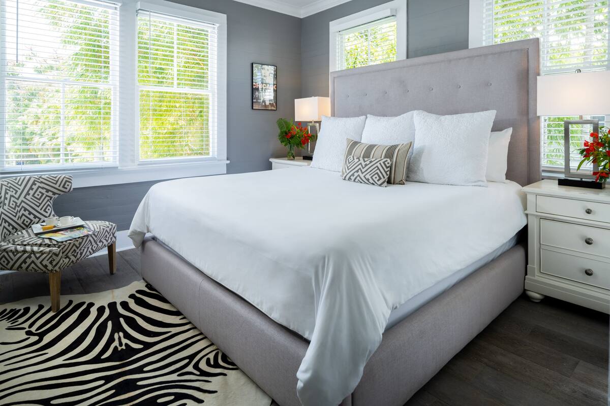 A bedroom with a large bed, a zebra-patterned rug, a chair, and a nightstand with a lamp.