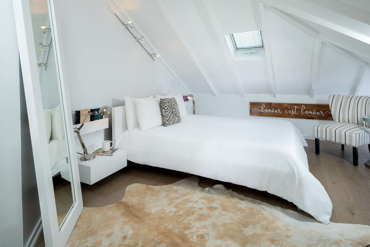 A bedroom with a bed, a bedside table, a mirror, a window, and a wall-mounted sign.