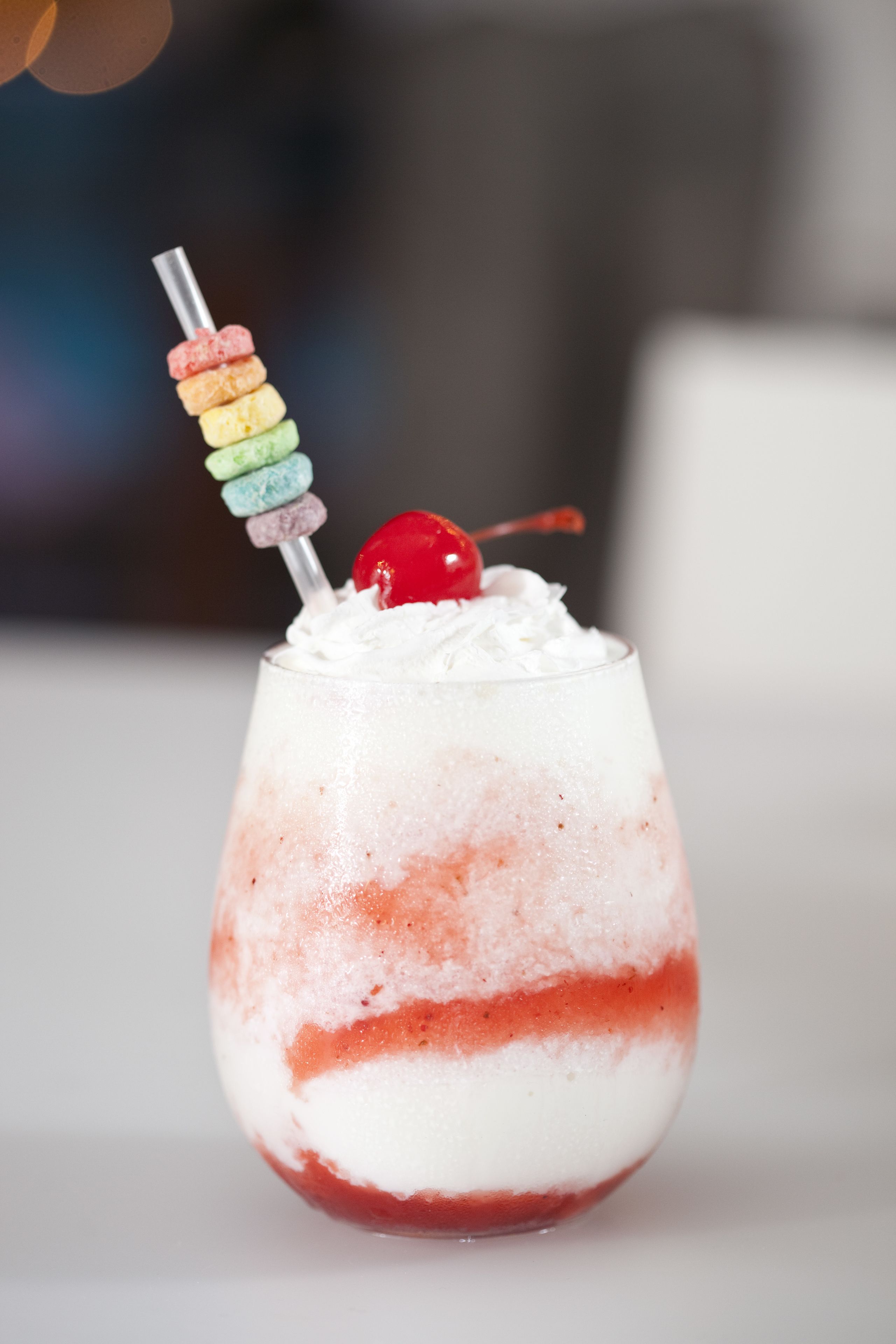 A layered cocktail with a cherry on top and colorful macarons on a skewer.
