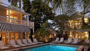 Zona de piscina con sillones reclinables, una piscina y un edificio con balcón y mobiliario exterior.