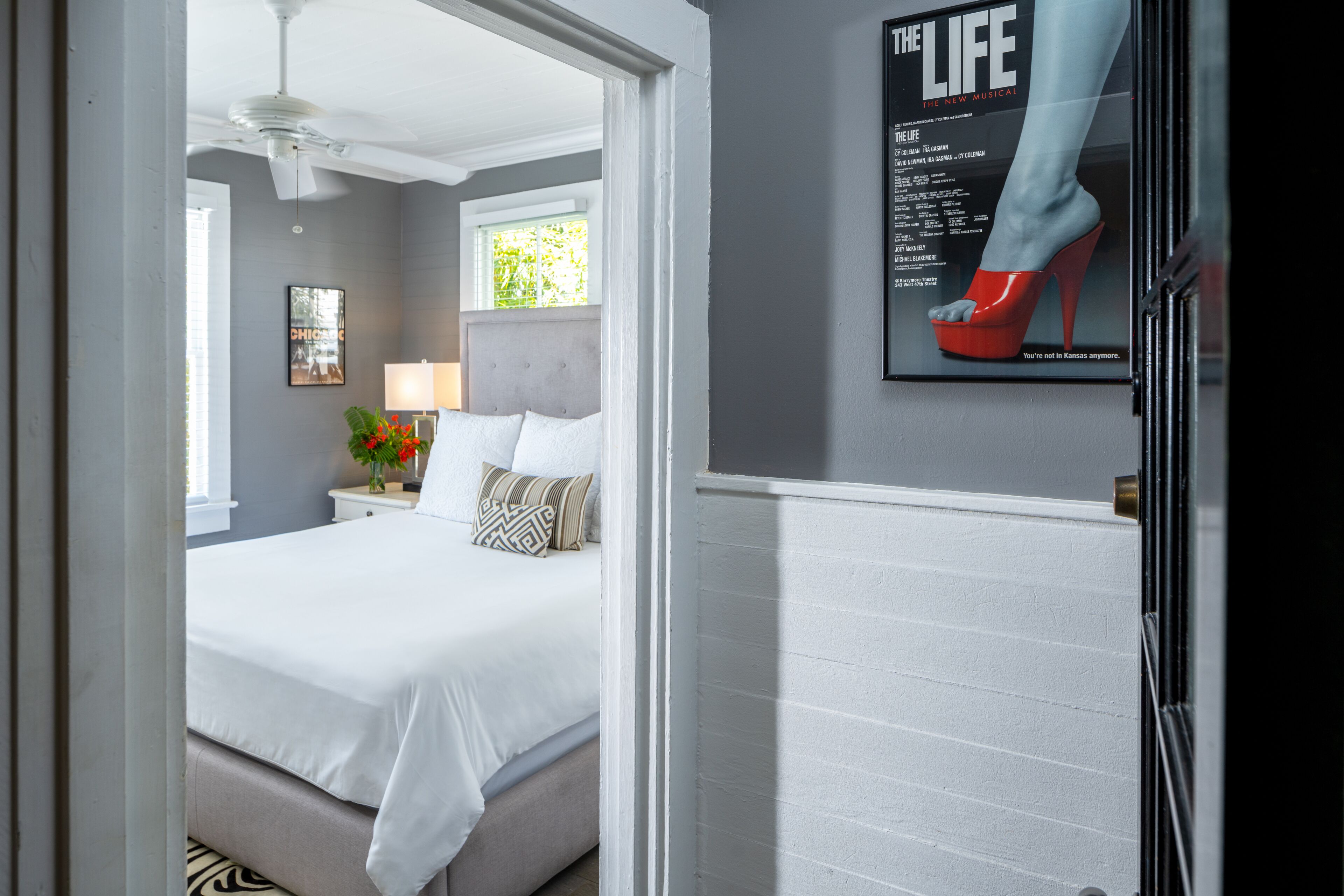 A bedroom with a bed, nightstand, lamp, and a poster of high heels.