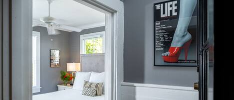 A bedroom with a bed, nightstand, lamp, and a poster of high heels.