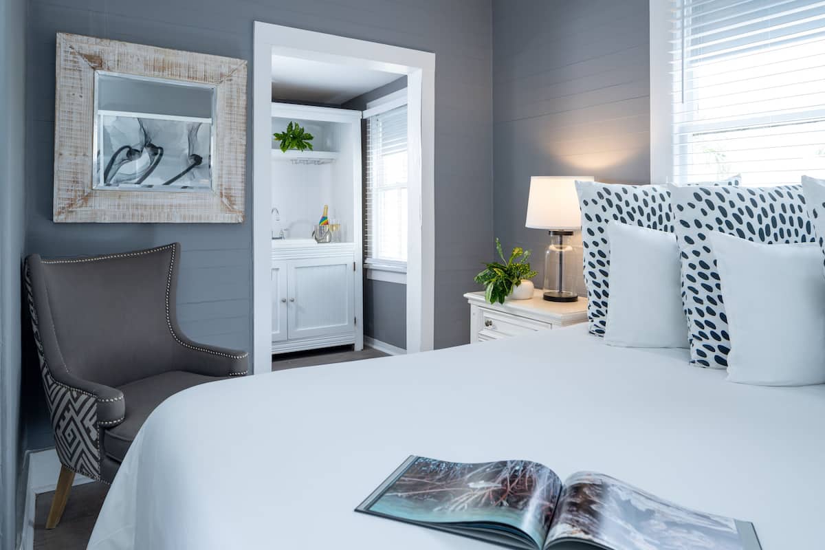 A modern hotel room with a large bed, a chair, a nightstand, and a mirror.