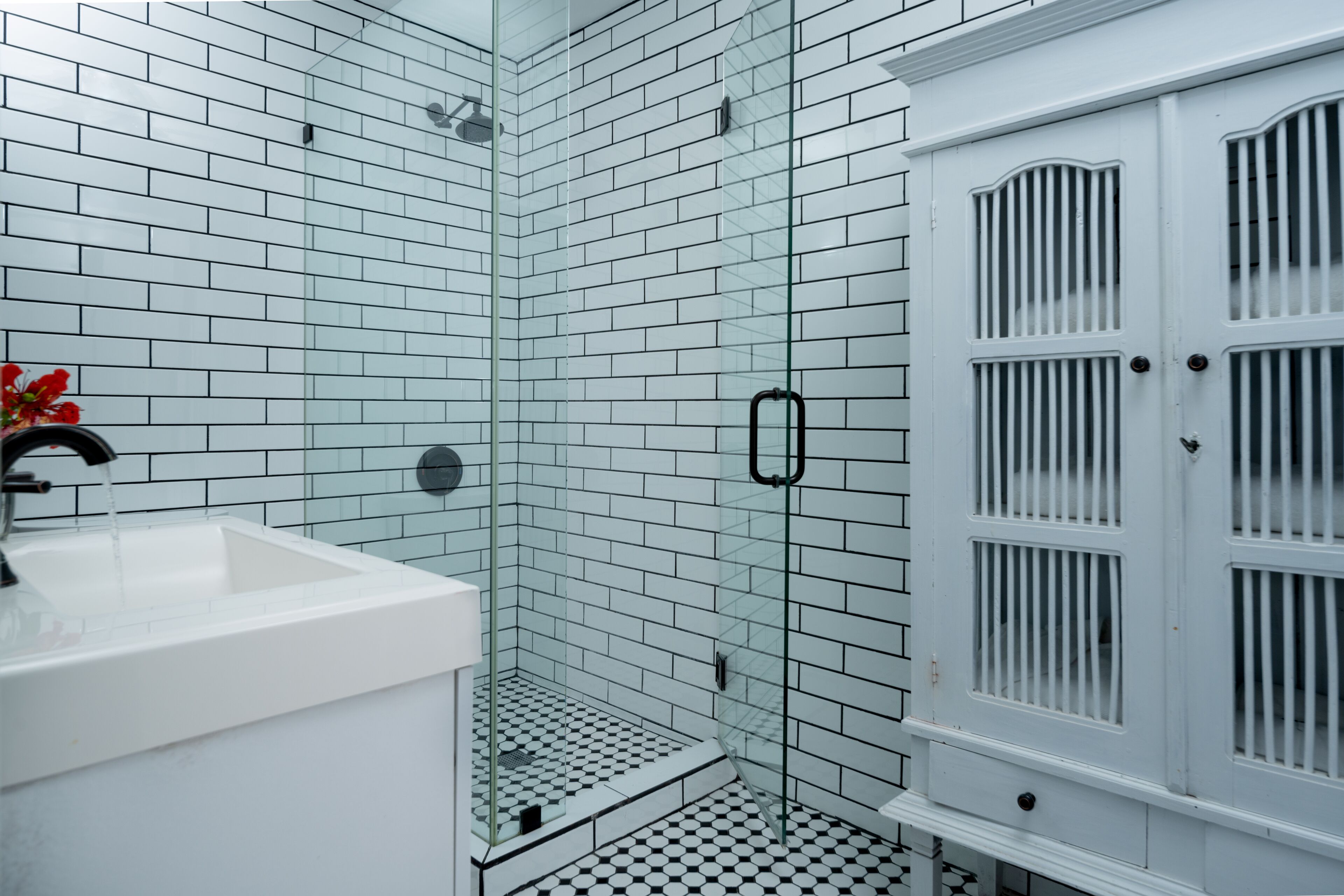 Un baño con azulejos blancos tipo metro, una cabina de ducha con mampara de vidrio y un mueble blanco con puerta.